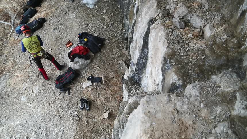 A man in a yellow vest puts on gloves near a rocky cliff
