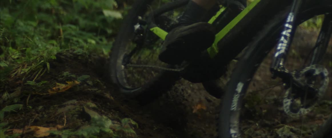 A cyclist sends up a cloud of dirt while making a sharp turn on a dirt trail in wilderness during the day