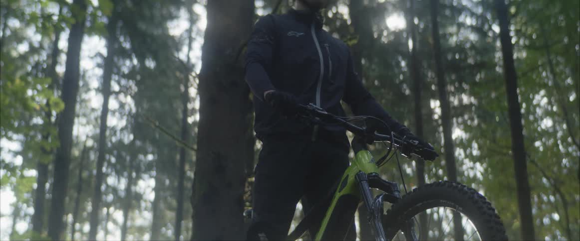 A man is sitting on a bicycle and looks ahead with forest behind him