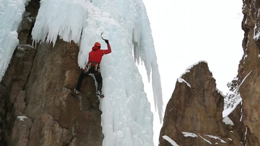A person in a red jacket climbs an icy cliff