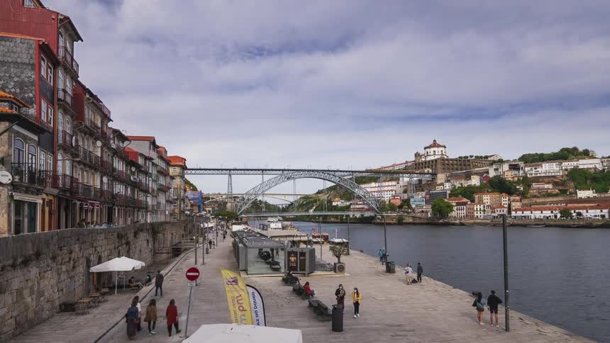 Many people walk along a dock on a river in a city