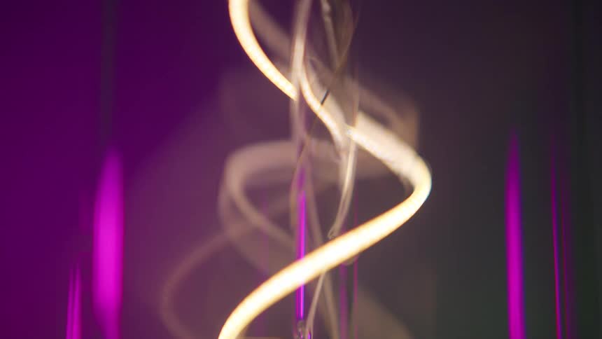 Light in background change color as small neon curved loop glows white amber as it loops around other translucent tubes