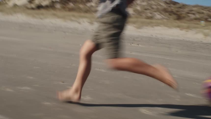 Young boy runs with an adult male as the adult kicks a ball in front of him
