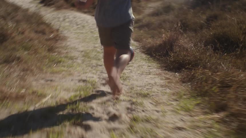 A child chases a ball on a sandy path into the brush