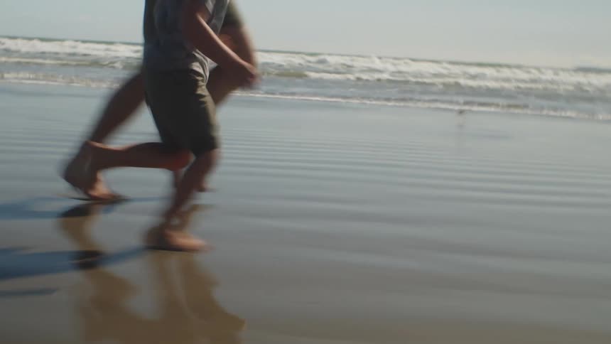 A man and boy run together across a beach on a sunny day