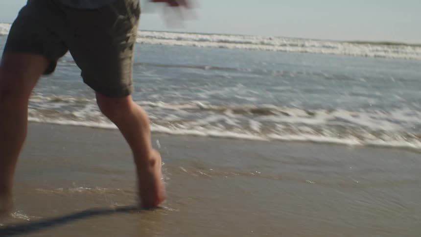 A man and a boy run around on a beach on a sunny day