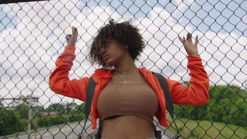 A model poses with her back against a fence on a highway overpass