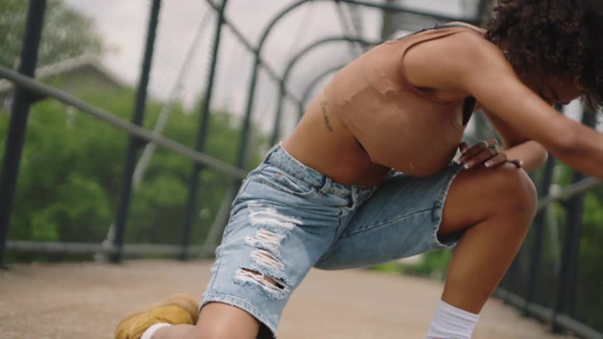 Woman performs dance moves on a fenced in bridge near the trees
