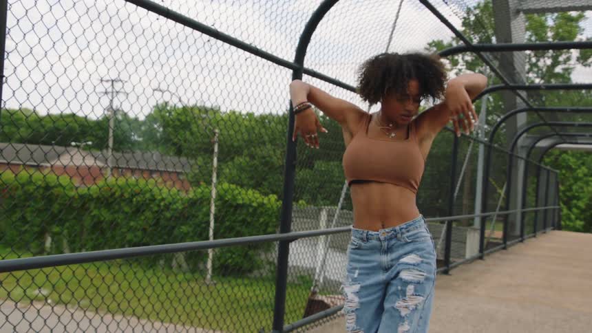 Woman wearing denim shorts dances on a bridge near the trees