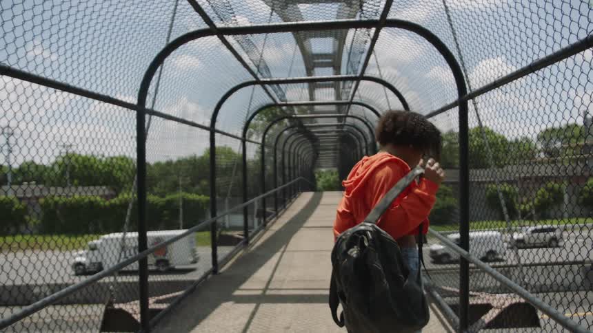 A woman on a pedestrian bridge over a highway takes off her backpack