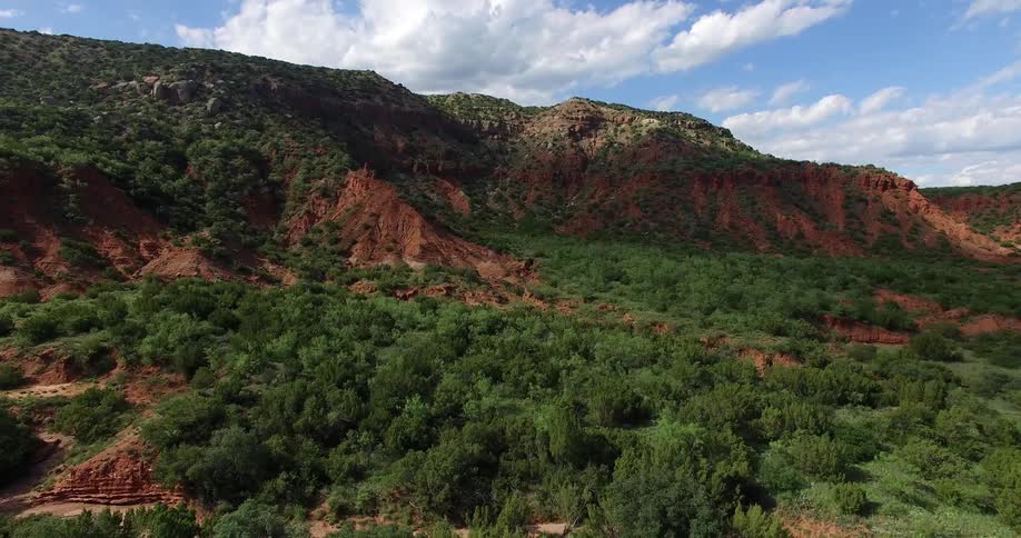 A red, rocky hill covered in green shrubs