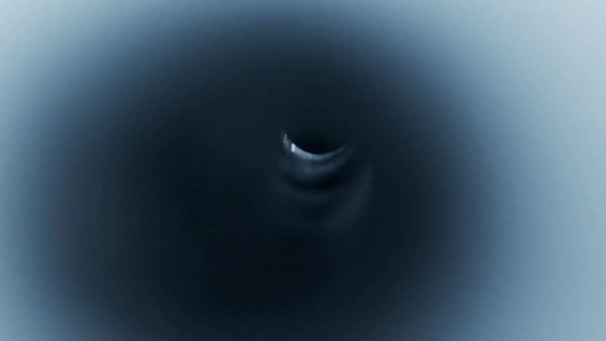 Liquid flows through a small tube and into a hole as ripples can be seeing along its surface