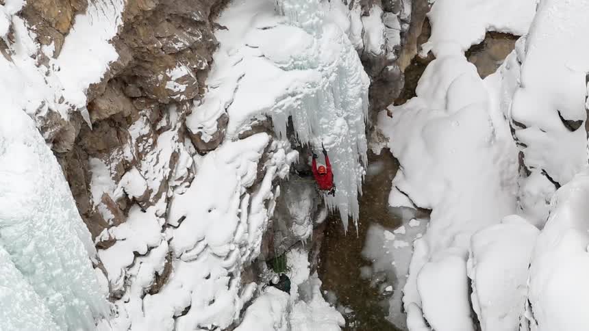 A person climbs a cliffside covered in snow and ice