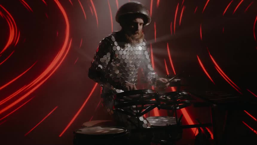 A male drummer plays his drum set in front of a projection screen with surreal imagery on it