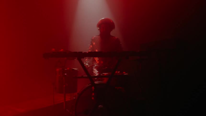 A man in a room playing the drums with drumsticks with a screen in the background