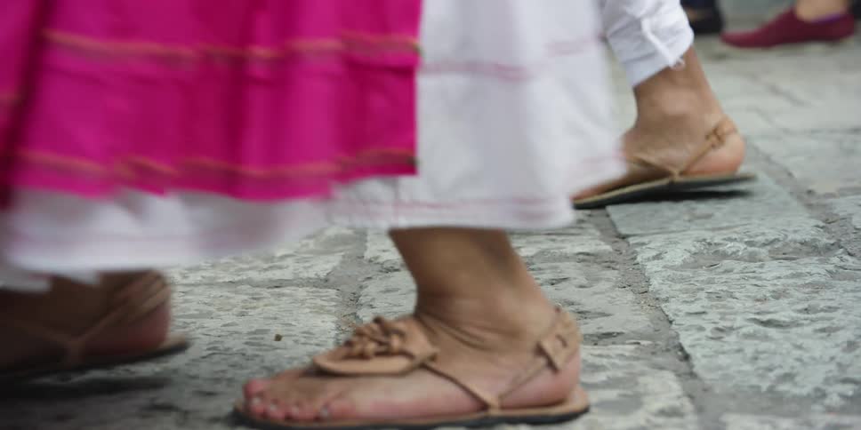 The feet of dancers in traditional garb as they dance on a stone street