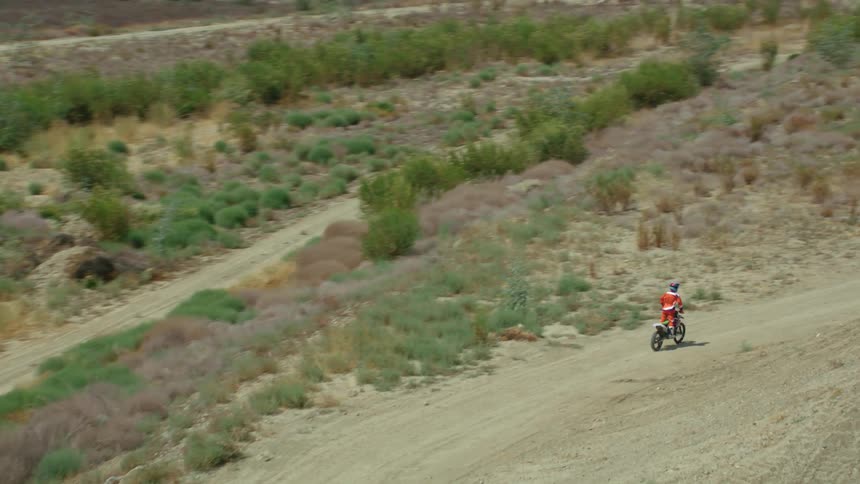 A cyclist stands up while riding a bicycle past a trick ramp in a dirt field