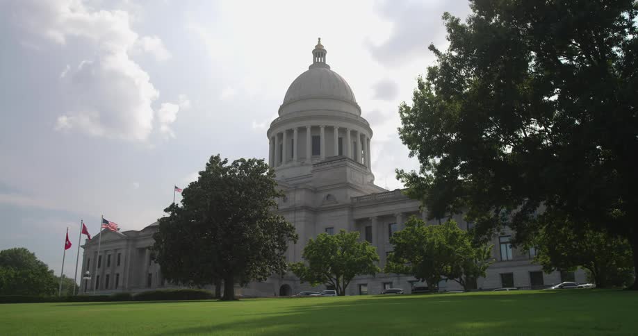 Large white building sits behind the trees as flags fly in front