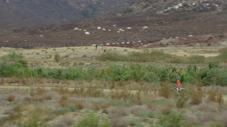 A person riding a dirt bike on an obstacle course with trees and a mountain range in the background