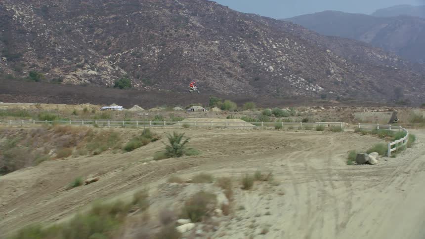 A person riding a dirt bike on an obstacle course with trees a mountain range the sky and clouds in the background