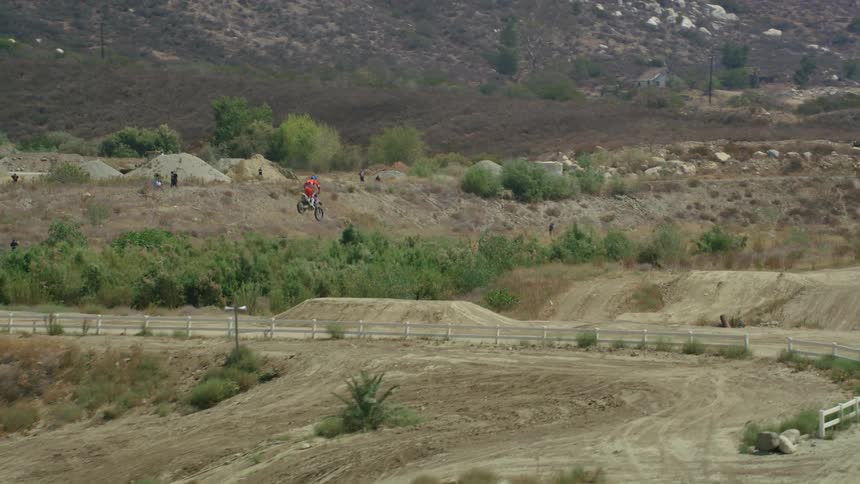 A person riding a motorbike on a dirt track goes over a large jump