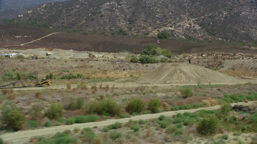 A bicyclist rides through an empty quarry surrounded by fields and tall hills