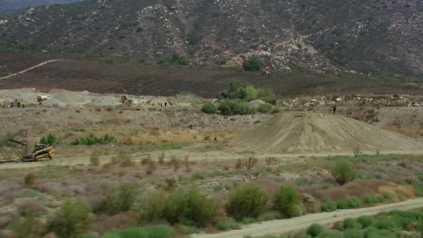 A bicyclists rides up a ramp and jumps onto a plateau and into an empty quarry
