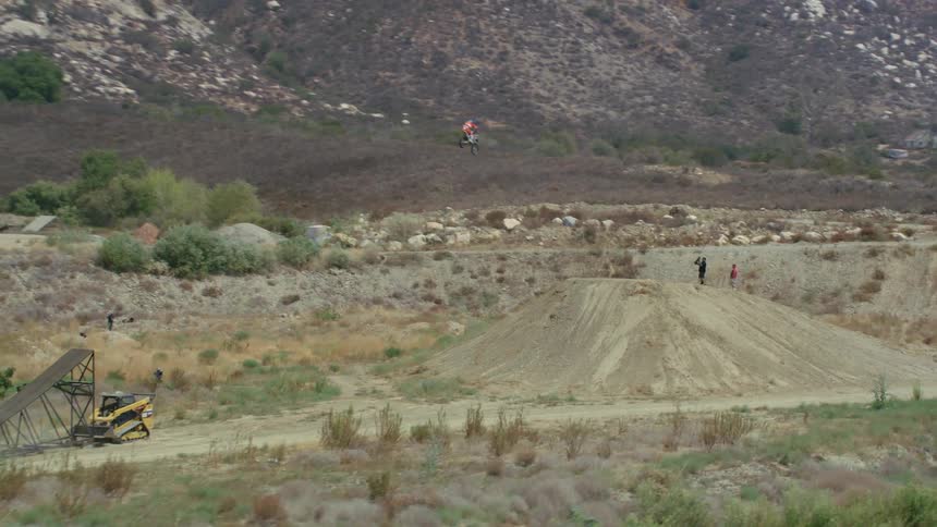 A dirt bike on a desert dirt road jumps off a ramp and over a mound