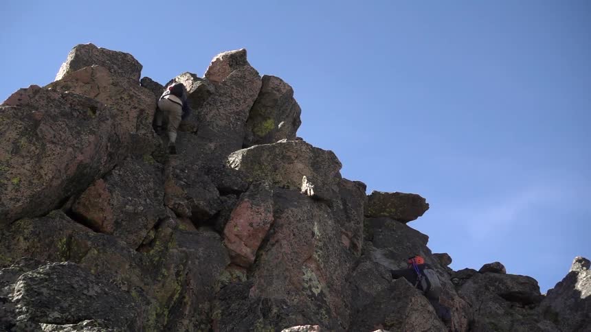 A man in khakis climbs a rocky cliff face