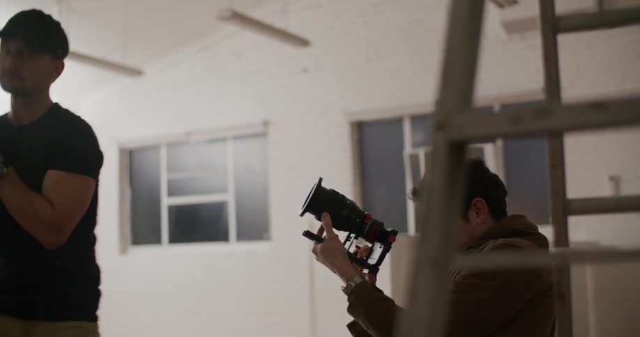 A man uses a digital camera to record footage in a studio as an assistant watches