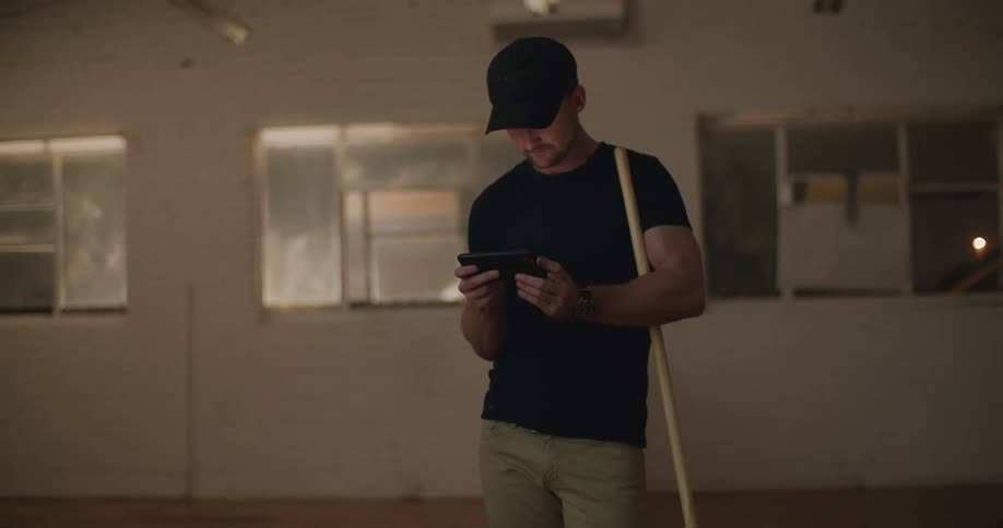 A janitor uses his smartphone while holding a mop in an empty room