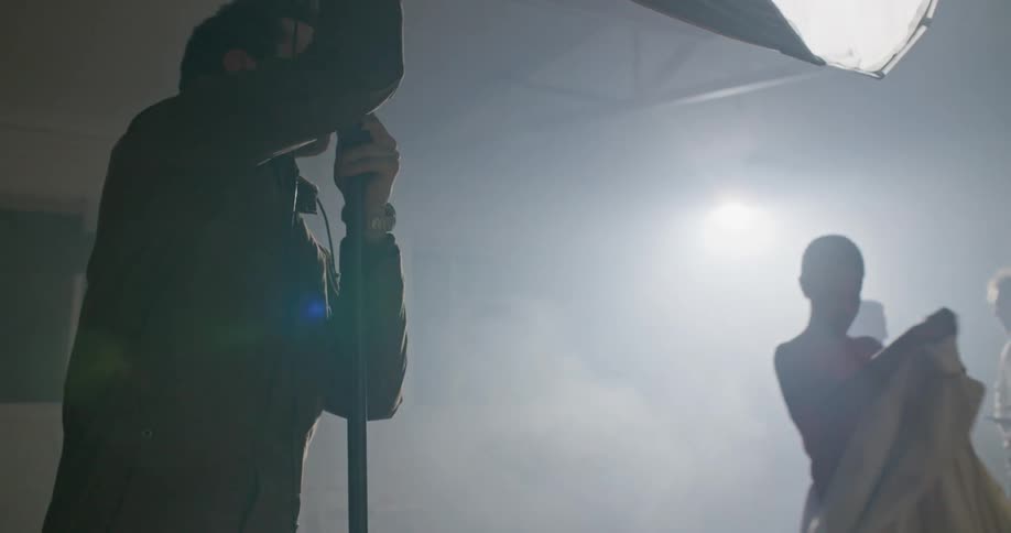 A man lowers a large umbrella light as a woman walks by carrying her coat