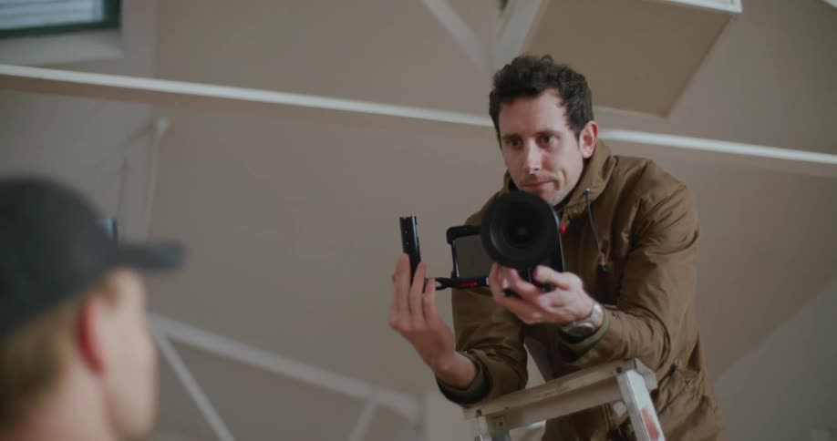 A photographer stands on a ladder holding his camera and instructs another man where to stand