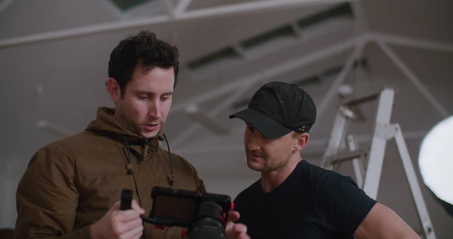 Two men review photos on a digital camera during a photoshoot