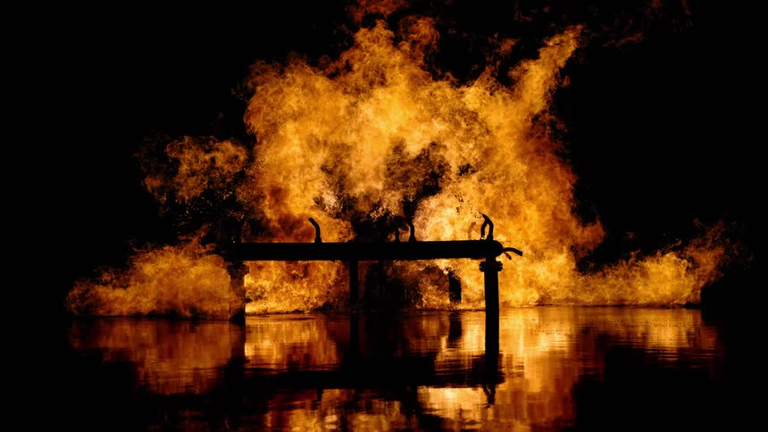 A structure is burning and the flames are reflecting on the water below