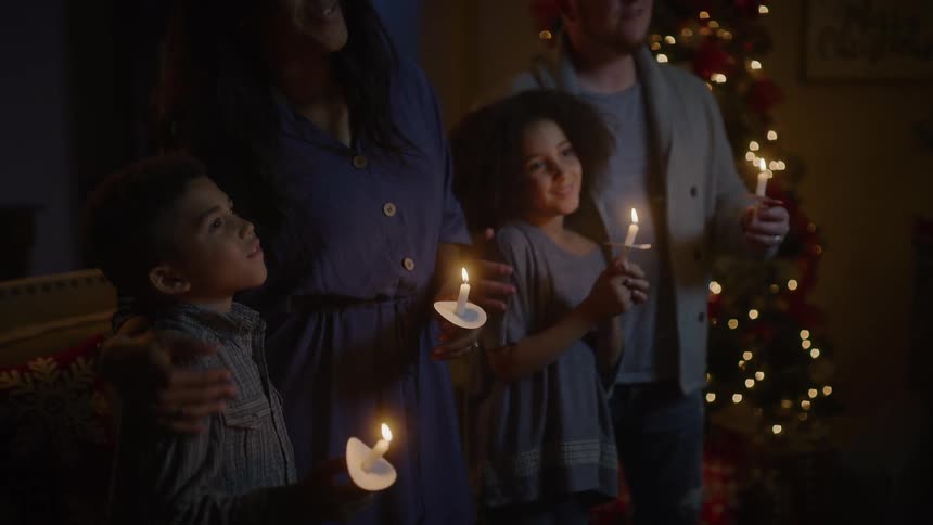 A family standing near a christmas tree holding candles