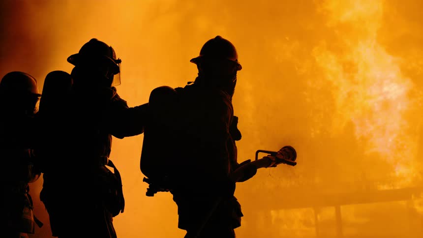 A group of firefighters spray a burning house with a firehose at night