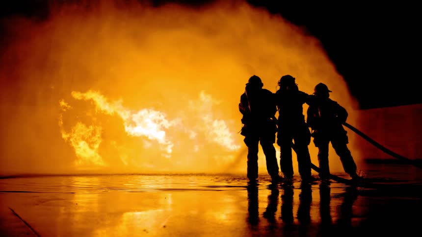 Silhouettes of firefighters battling huge flames