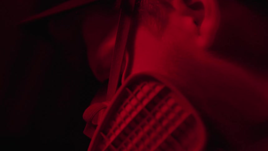 A man faces a protective gas mask while working in a dark room with a red glowing light