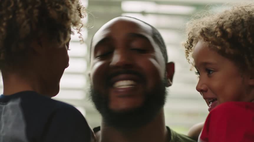 Smiling father holds and talks to his children near window