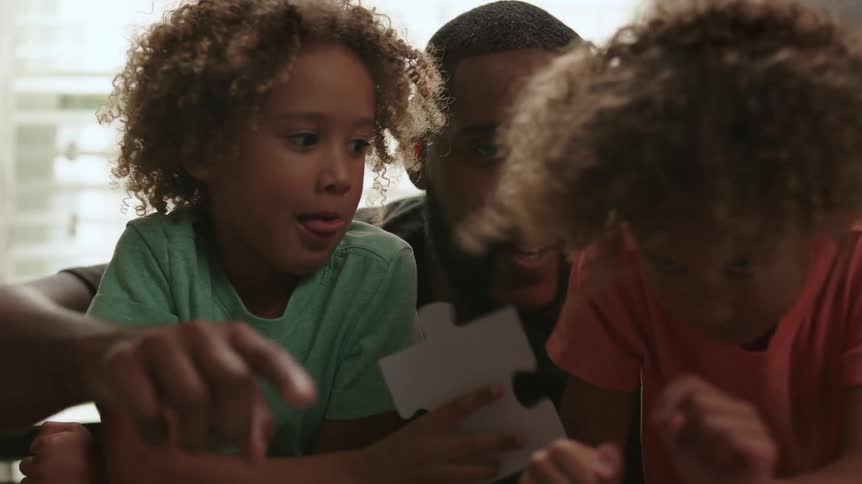 A father sits beside his two children one of them holding a large puzzle piece