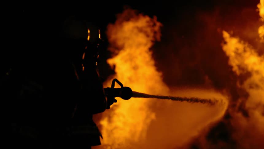 Firefighter dousing a raging fire with water at night