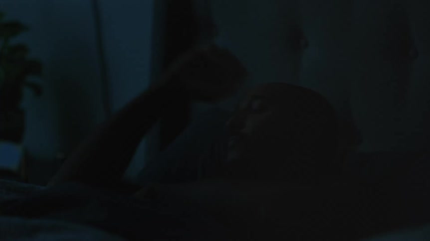 A man in a bedroom laying in a bed with a wall and a window in the background