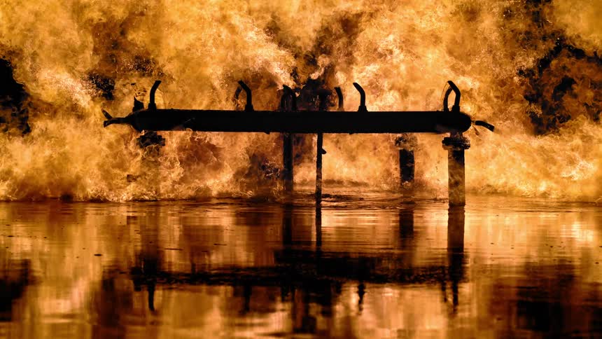 A structure is burning and the flames are reflecting on the water below