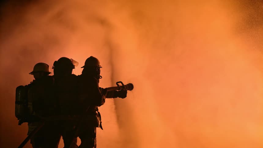 A silhouette of three firefighters holding a hose spraying water