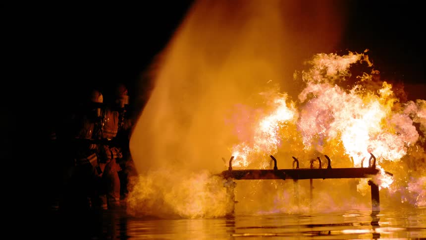 A small group of firefighters aim a fire hose at a raging fire
