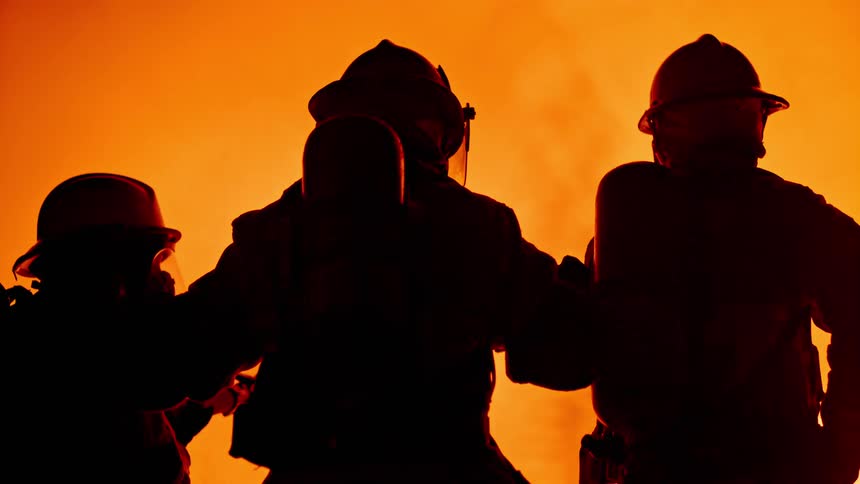 A silhouette of three firefighters with masks and helmets with a fire in the background