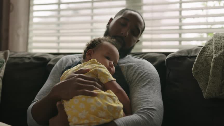 A man sits on a couch holding a baby girl