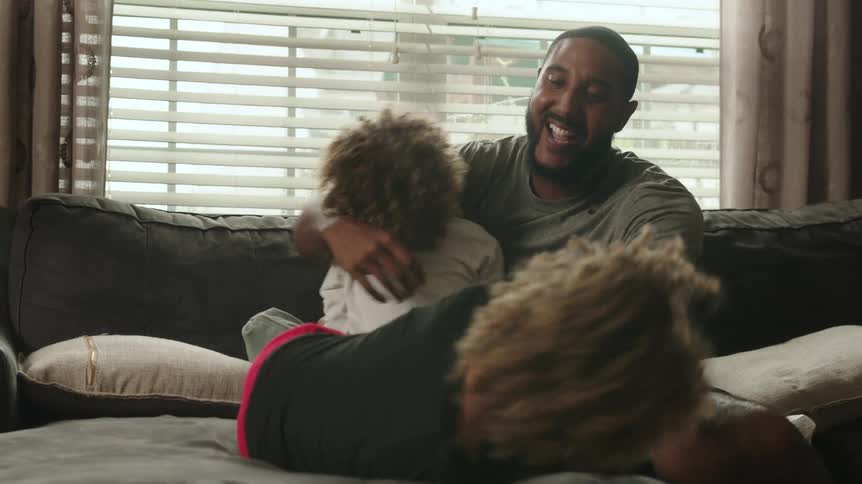 Happy father tickling his sons on the couch in the living room at home