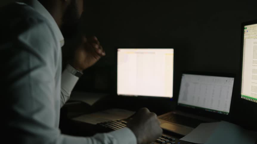 A man in a room sitting at a desk with computers and a laptop